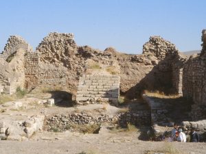 <p>Fig. 12. Remains of the south eyvān of the fire temple complex in 1994. The group of people right is standing on the floor of the Sasanian period, some 70 cm below. The whole area had been concealed under a thick layer of limestone deposit left by repeated overflooding of the lake (photo: A, Mousavi)</p>
